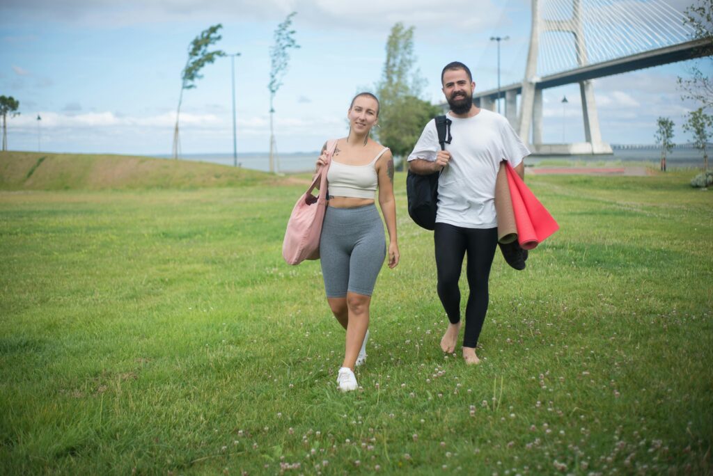 Couple walking in Lisbon park with yoga mats, showcasing active lifestyle in natural setting.