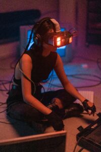 A woman sits cross-legged wearing VR headset and gloves in a futuristic setting.