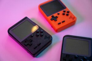 A vibrant still life of retro handheld game consoles in varying colors, set against a soft background.