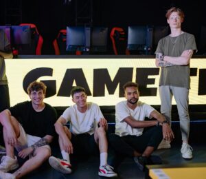 Four young men posing confidently in an eSports arena with gaming setups in the background.