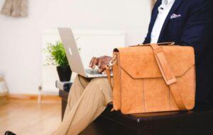 A stylish businessman working on a laptop indoor with a leather briefcase.