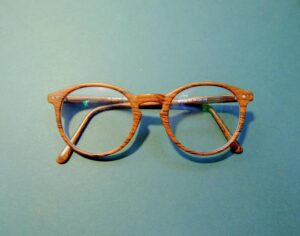 Close-up of fashionable wooden frame eyeglasses on a solid blue background.