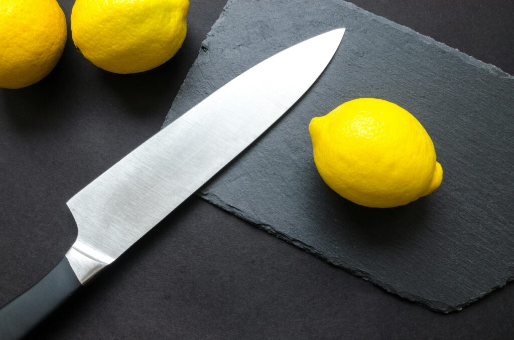 Top view of juicy lemons and a sharp kitchen knife on a slate board, perfect for culinary themes.