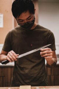 An adult man sharpening a knife indoors, emphasizing safety and precision.