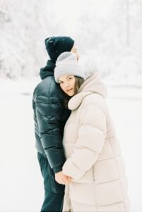 A young couple embraces warmly in a winter wonderland, dressed in cozy coats.