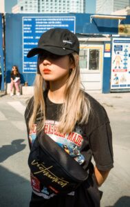 Young woman in casual streetwear with cap and fanny pack outdoors on a sunny day.