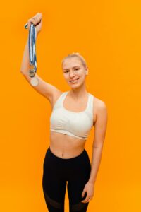 Sporty woman smiling and holding up a silver medal against an orange background in studio.