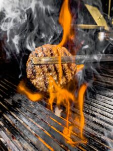 Close-up of a burger patty being grilled with flames and smoke for a mouth-watering look.